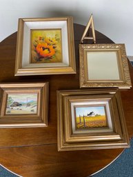 Four Small To Medium Pieces Of Artwork And A Gold Color Framed Mirror With Stand