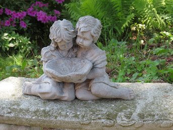 A Concrete Statue Of A Boy And Girl Holding A Leaf Bowl Between Them.