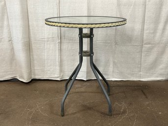 A Small Glass Topped Bistro Table With Braided Trim