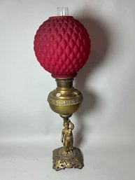 A FIGURAL BRONZE OIL LAMP W/ A QUILTED RUBY GLASS SHADE