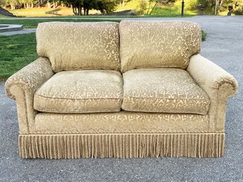 A Charming Upholstered Rolled Arm Loveseat With Fringe Skirting