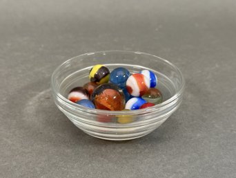 A Small Glass Bowl With A Handful Of Glass Marbles