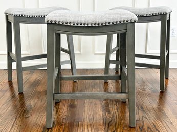 A Trio Of Modern Saddle Stools In Grey Linen With Nailhead Trim