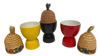 A Trio Of Bright Ceramic Egg Cups With Straw Warmer Tops.