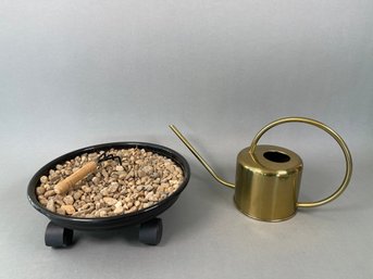 A Brass Toned Watering Can & Stones In Plant Dolly