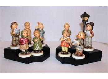 Nine Hummel Singing Figurines & Two Black Wood Tiered Stands