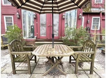 A Weathered Teak Dining Table, Pair Of Arm Chairs, And Striped Patio Umbrella