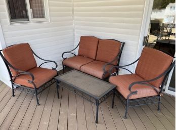 FOUR PIECE PATIO SET WITH IRON & GLASS TABLE, TWO SEAT SOFA & TWO ARM CHAIRS WITH ORANGE CUSHIONS