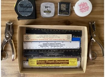 A Grouping Of Home Office Supplies Including Single Hole Punch, Measuring Tape And Rulers