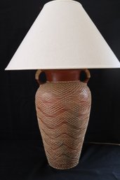 Tall Ceramic Double Handled Jar Lamp With Intricate Rattan Webbing And Linen Shade.