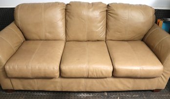 A Three Seat Tan Leather Sofa With Double Stitched Seams And Boxy Wooden Feet.