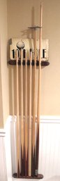 4 Cue Sticks And 2 Helper Cues On A Wall Mounted Rack.