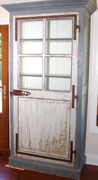 A Rustic Painted Blue Cabinet With Antiqued Rust Hinges And Glass Top Door.