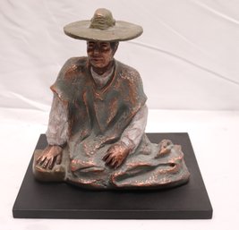Resin Figurine Of Seated Woman With Hat And Long Dress On Black Base.