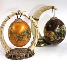 Two Decorative Painted Ostrich Eggs With Safari Scenes From South Africa Held On By A Faux Tusk