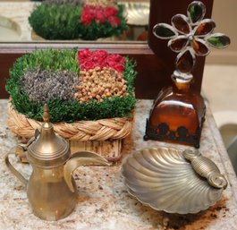 Assorted Decorative Items With Amber Glass Bottle On Metal Stand, Small Brass, Teapot, And Potpourri Basket.