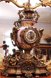 Elaborate French Style Gilded Clock With Floral Painted Porcelain Urn And Cherubs.