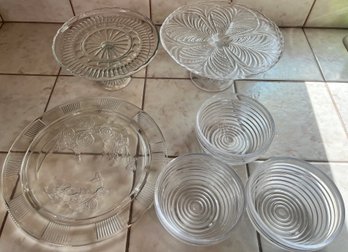 2 Glass Pedestal Cake Plates, 1 Glass Platter And 3 Acrylic Bowls.