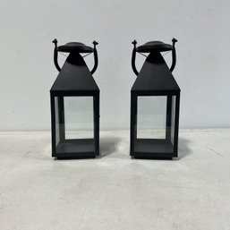 A Pair Of Small Black Metal Lanterns With Long Handles