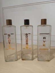 3 Clear Bottles. One Labled 'Scotch, One 'Bourbon' And The Last 'Rye'